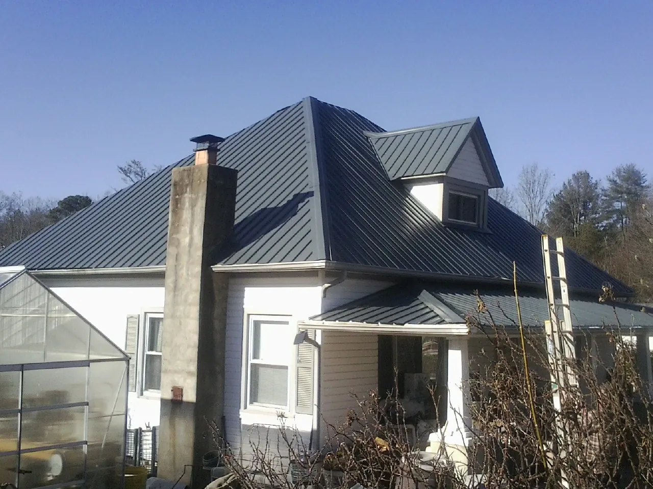 Dark blue standing seam metal roof on a white farmhouse with dormer — Slate & Tile Roof Repair by Roofing Brothers in Strafford
