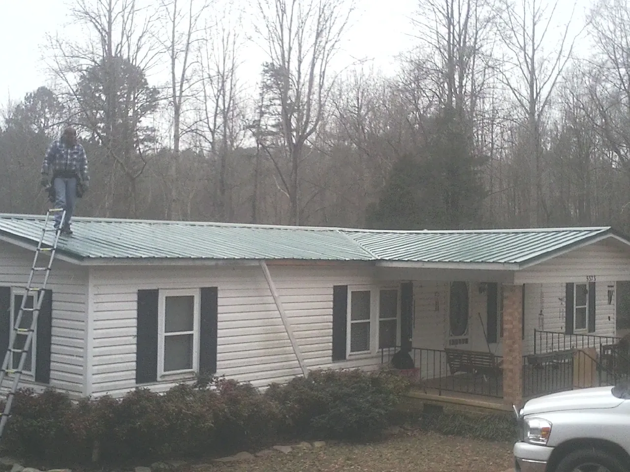Worker on a ladder beside a new green metal roof on a ranch home in Strafford