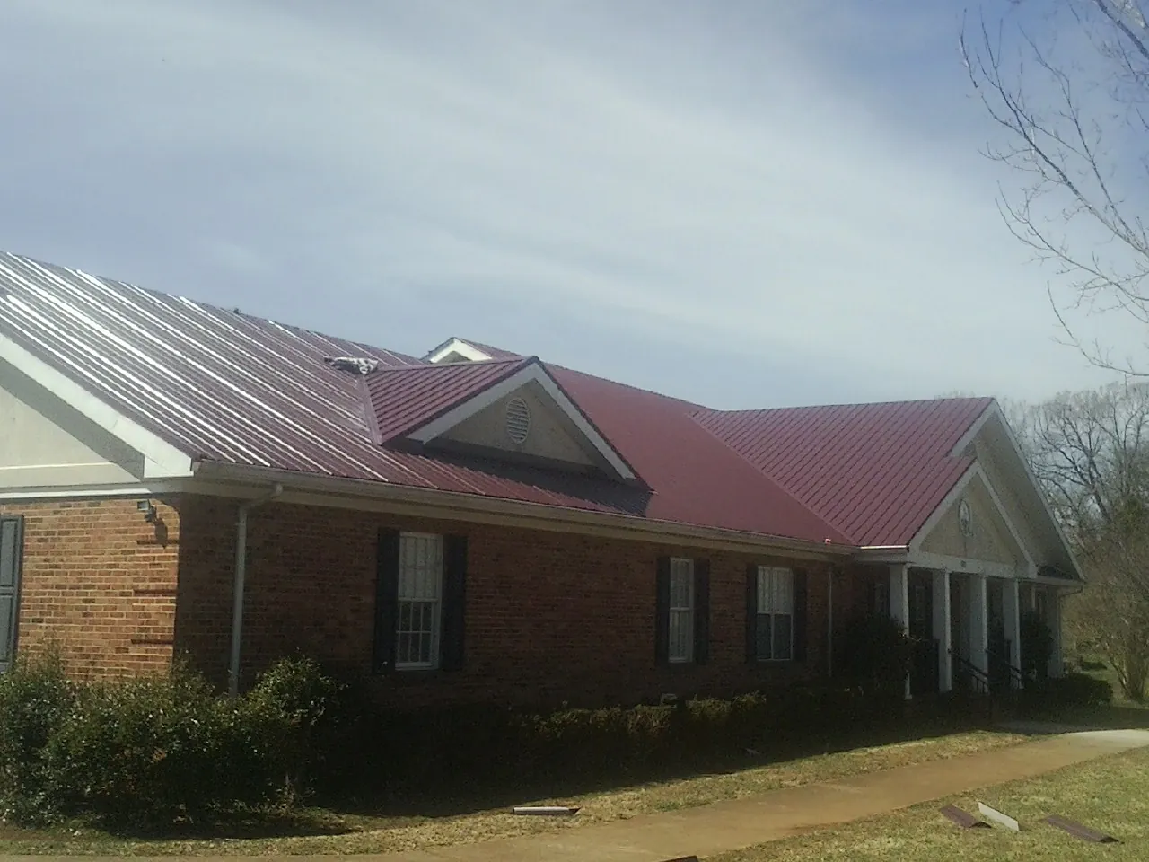 Red metal roof with gabled entries on a long brick building, from a Hail Damage Roof Repair job in Strafford
