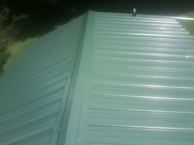 New green metal panels meeting at the ridge of a roof — Flat Roof Repair work by our crew in Strafford