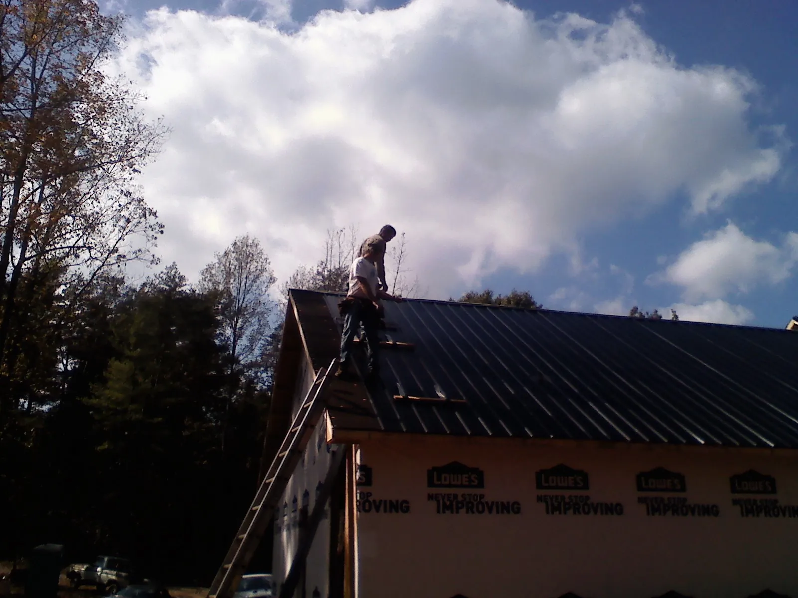 Roofer fastening dark metal panels high against a cloudy sky, from a Roof Inspection job in Strafford