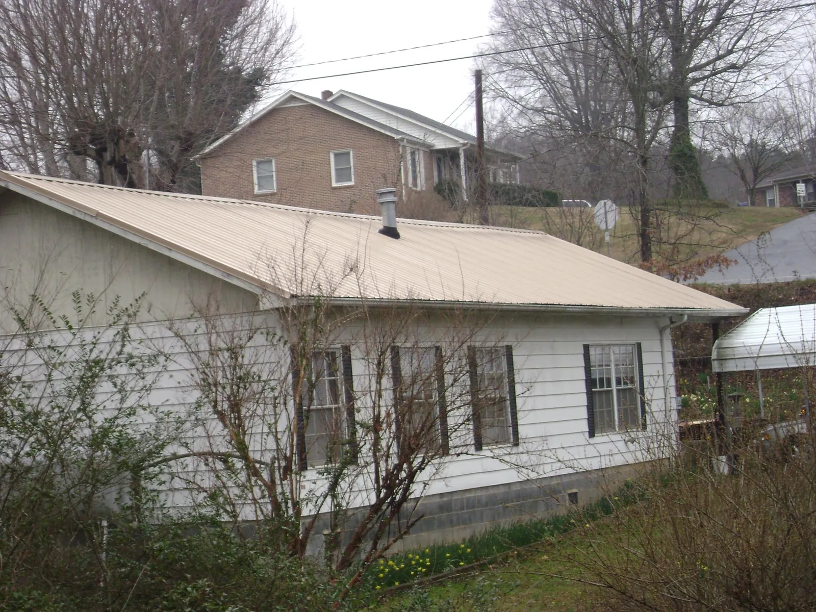 Tan metal roof on a white sided house set into a hillside — Commercial Roofing by Roofing Brothers in Strafford