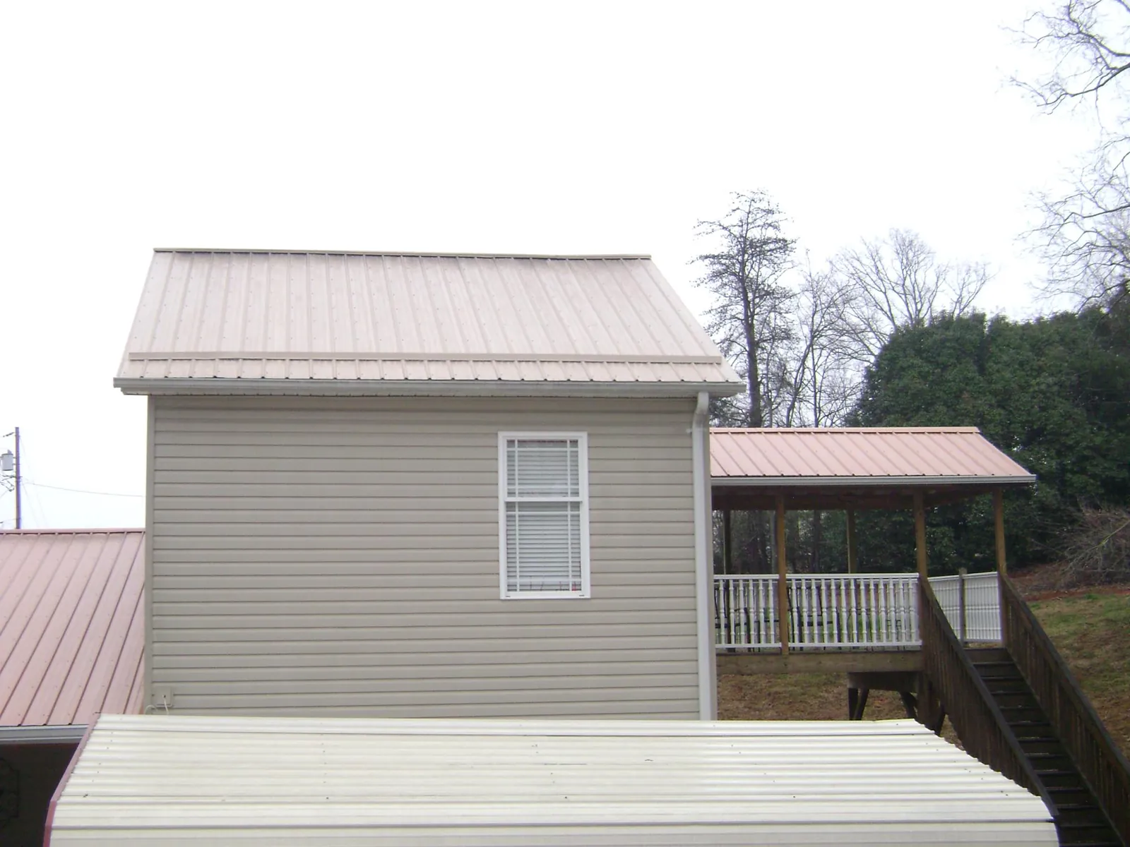 Tan metal roofs on a two story addition and attached porch, from a Roof Replacement job in Strafford
